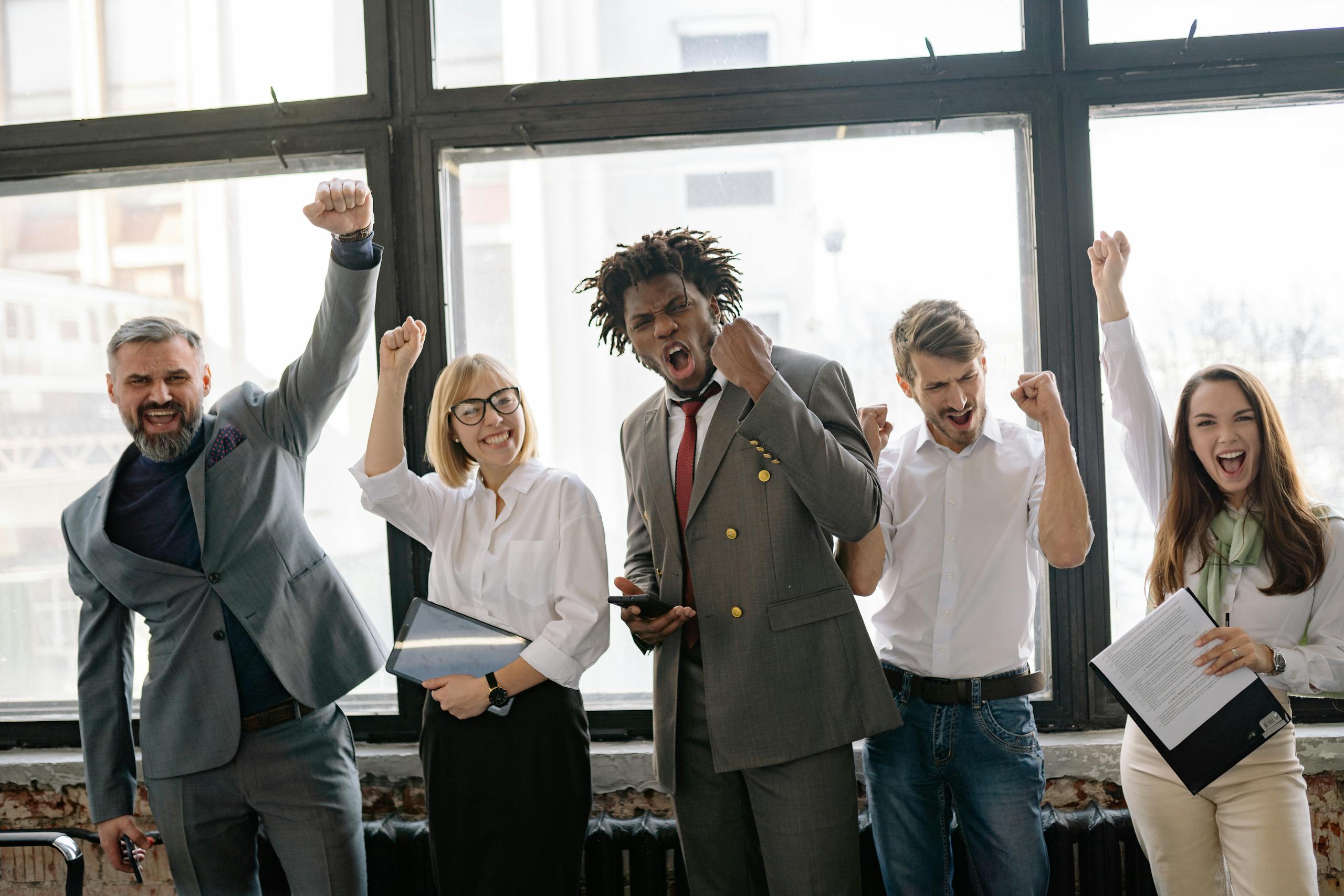 A group of diverse professionals celebrating achievement in office setting with enthusiasm.