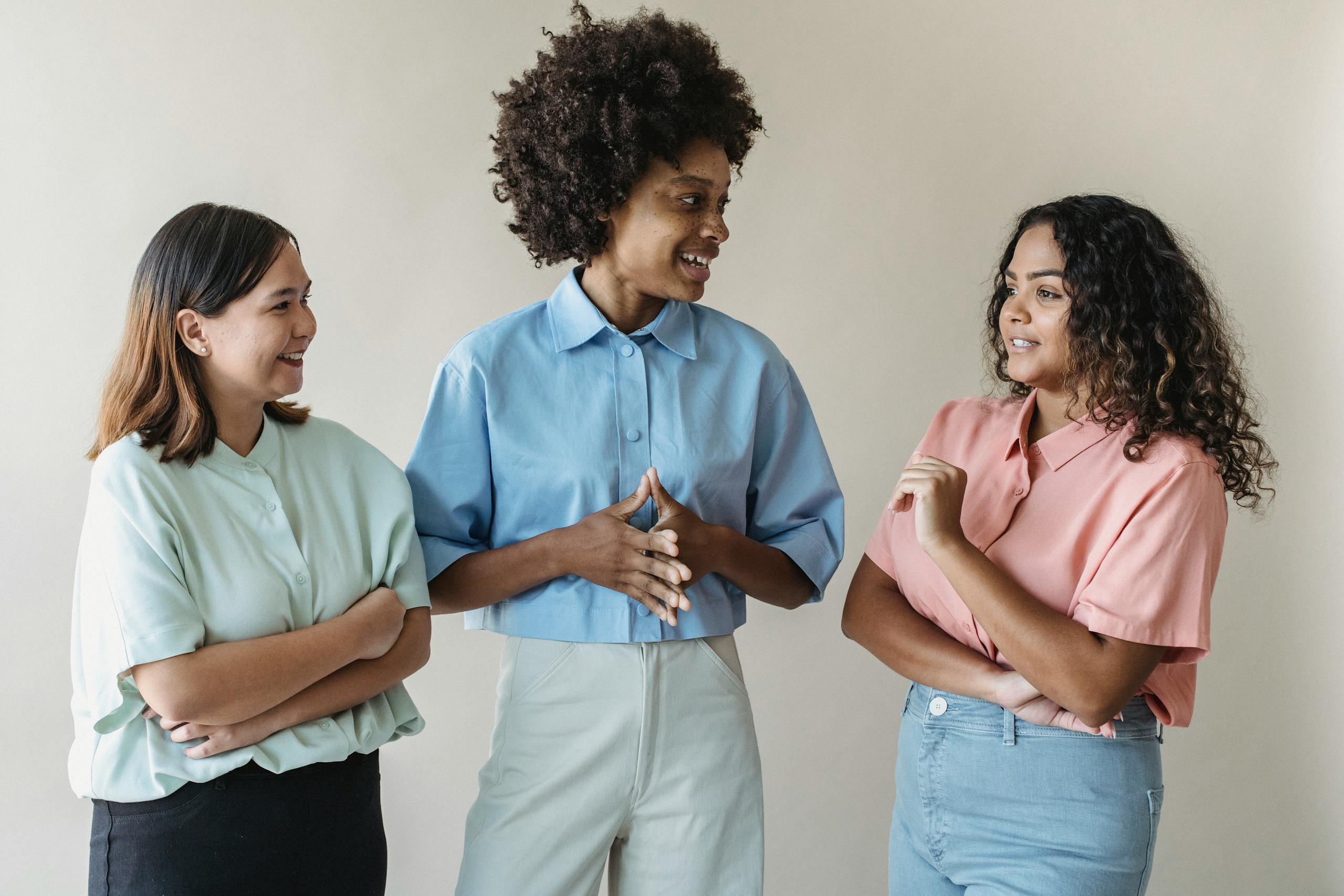 Group of diverse women smiling and talking, showcasing casual fashion in an indoor setting.