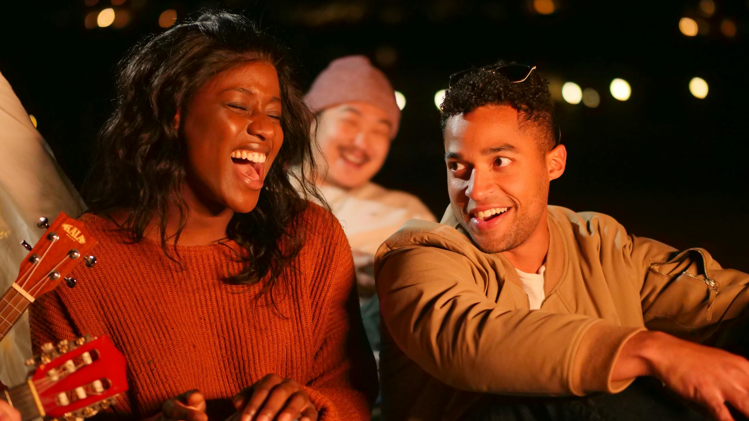 Group of friends enjoying a lively beach gathering with music and laughter at night.