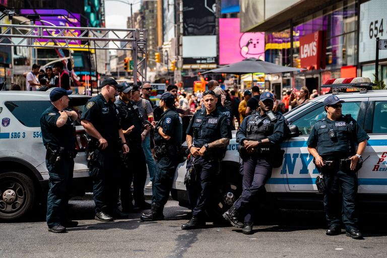 Group of NYPD officers standing by police cars in busy Times Square.