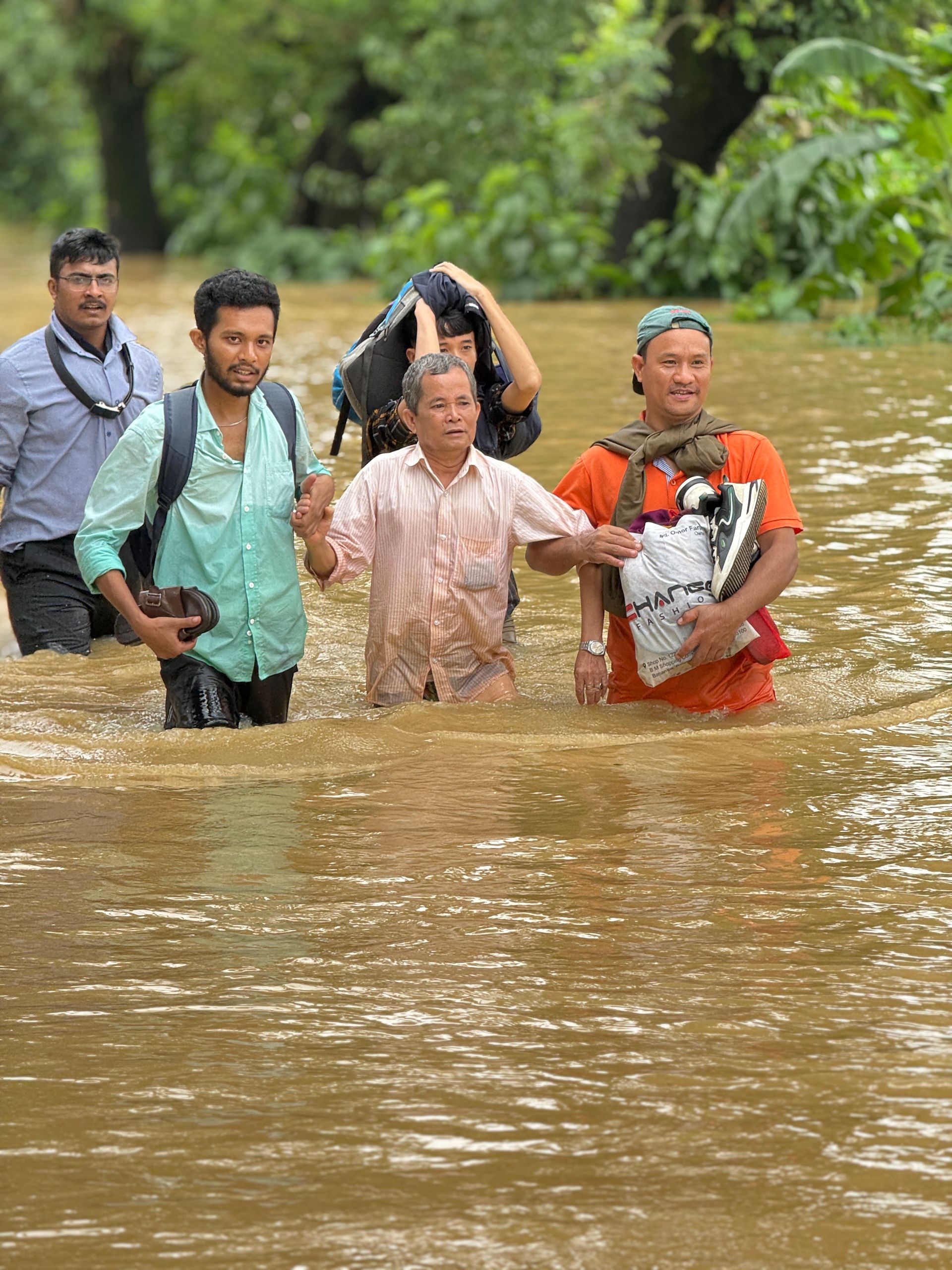 Group of people wading through floodwaters, assisting each other.