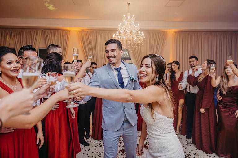 Happy couple and guests raise glasses for a joyful wedding toast indoors.