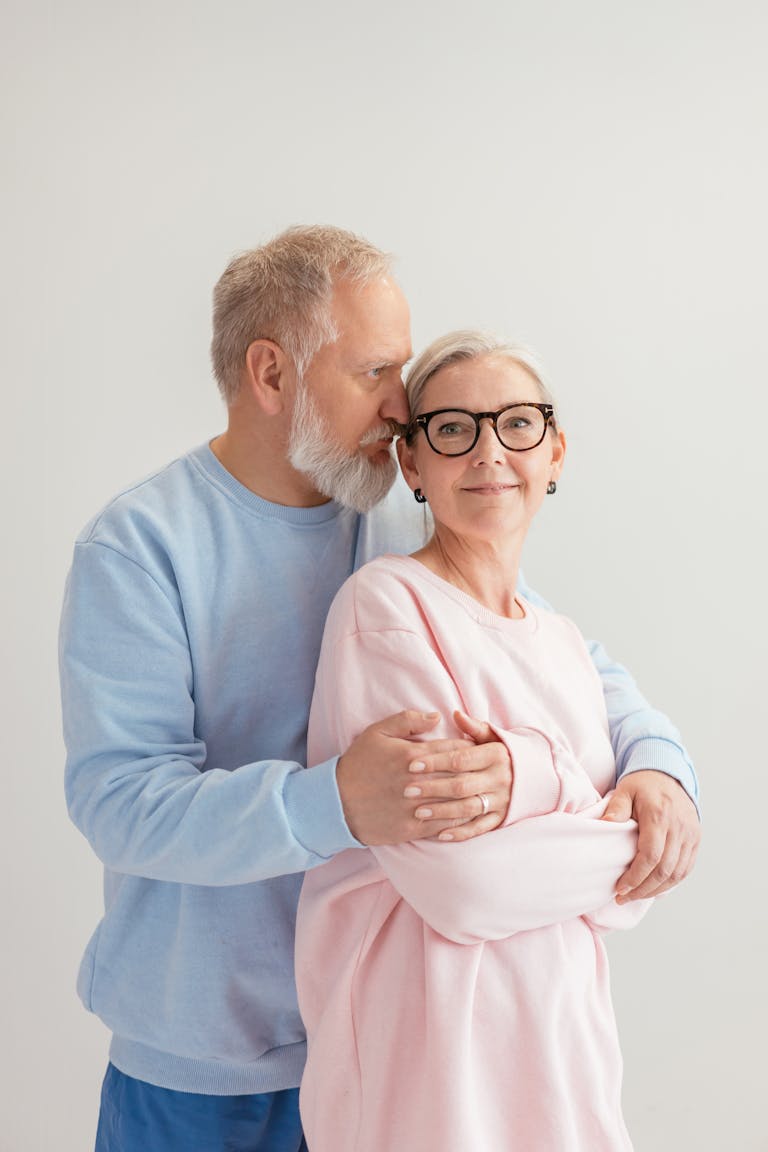 Happy senior couple embracing indoors in bright clothing against a white background.