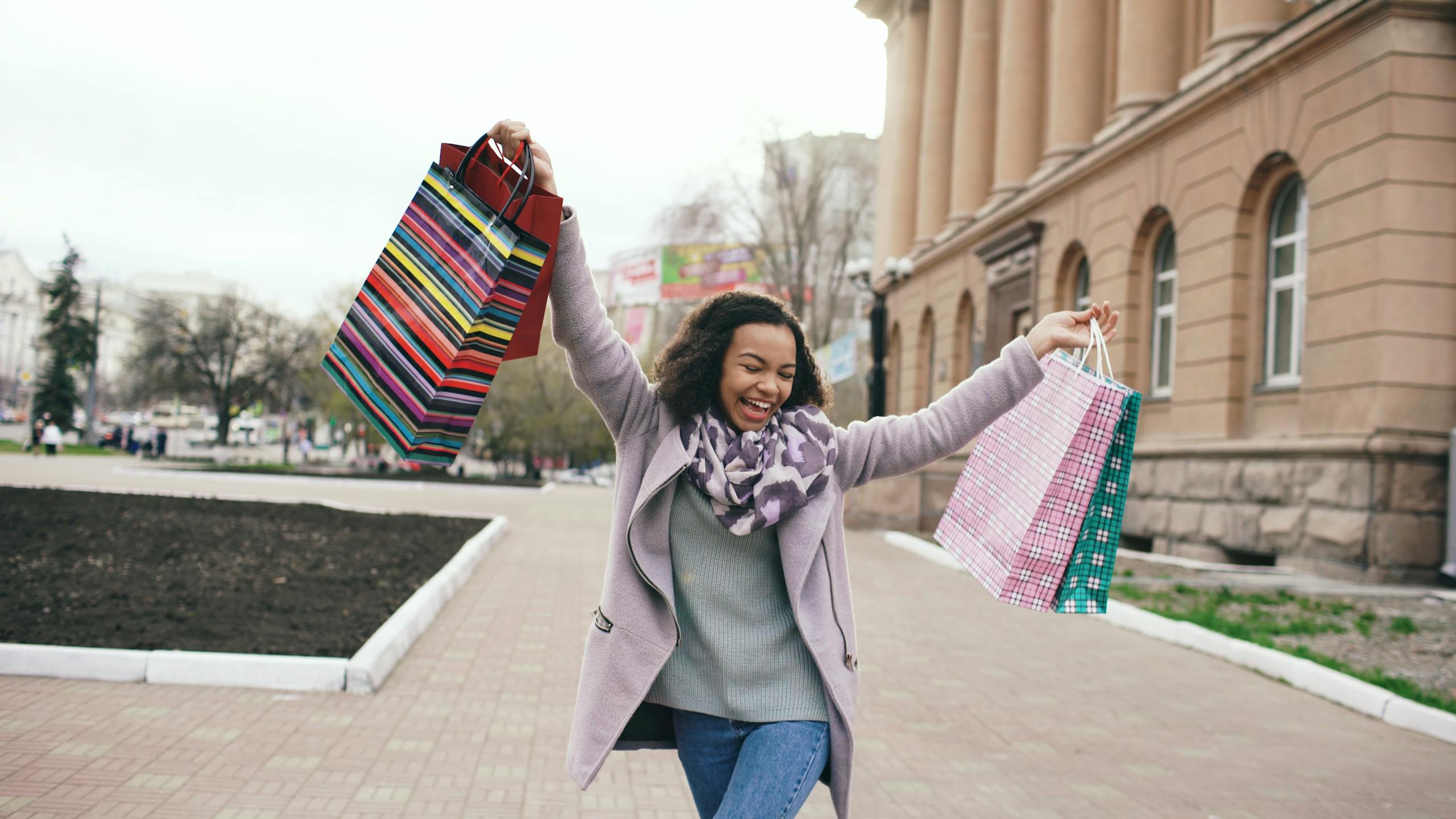 Happy woman holding shopping bags in city on a cool day.