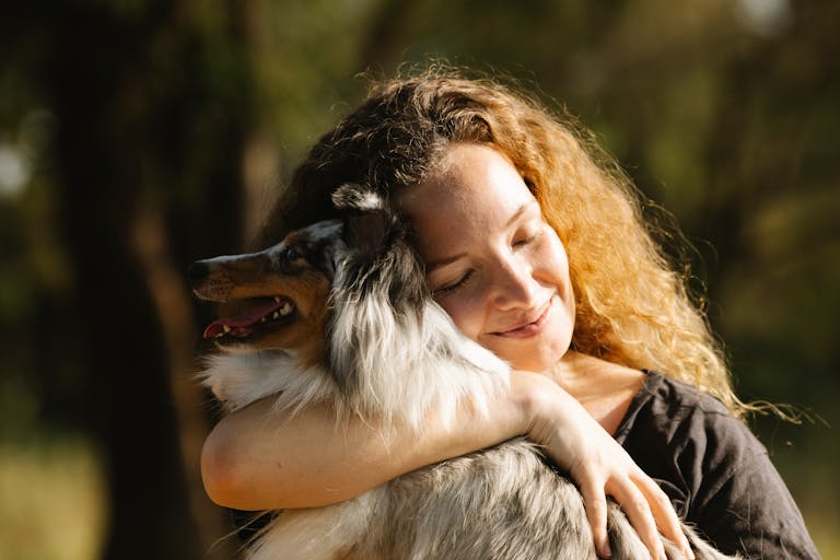 Happy woman hugging a Shetland Sheepdog in a sunny outdoor setting.