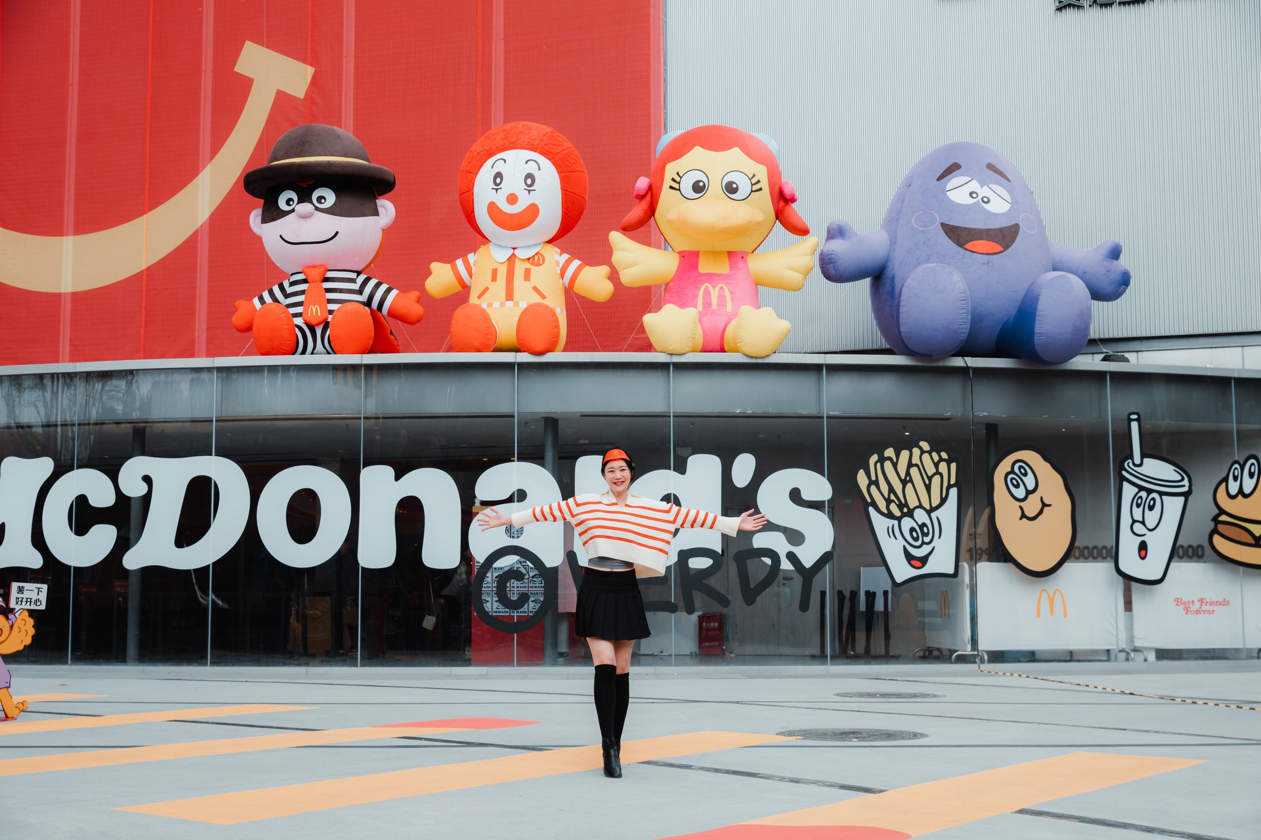 Happy woman posing in front of a McDonald's entrance with iconic character inflatables overhead.