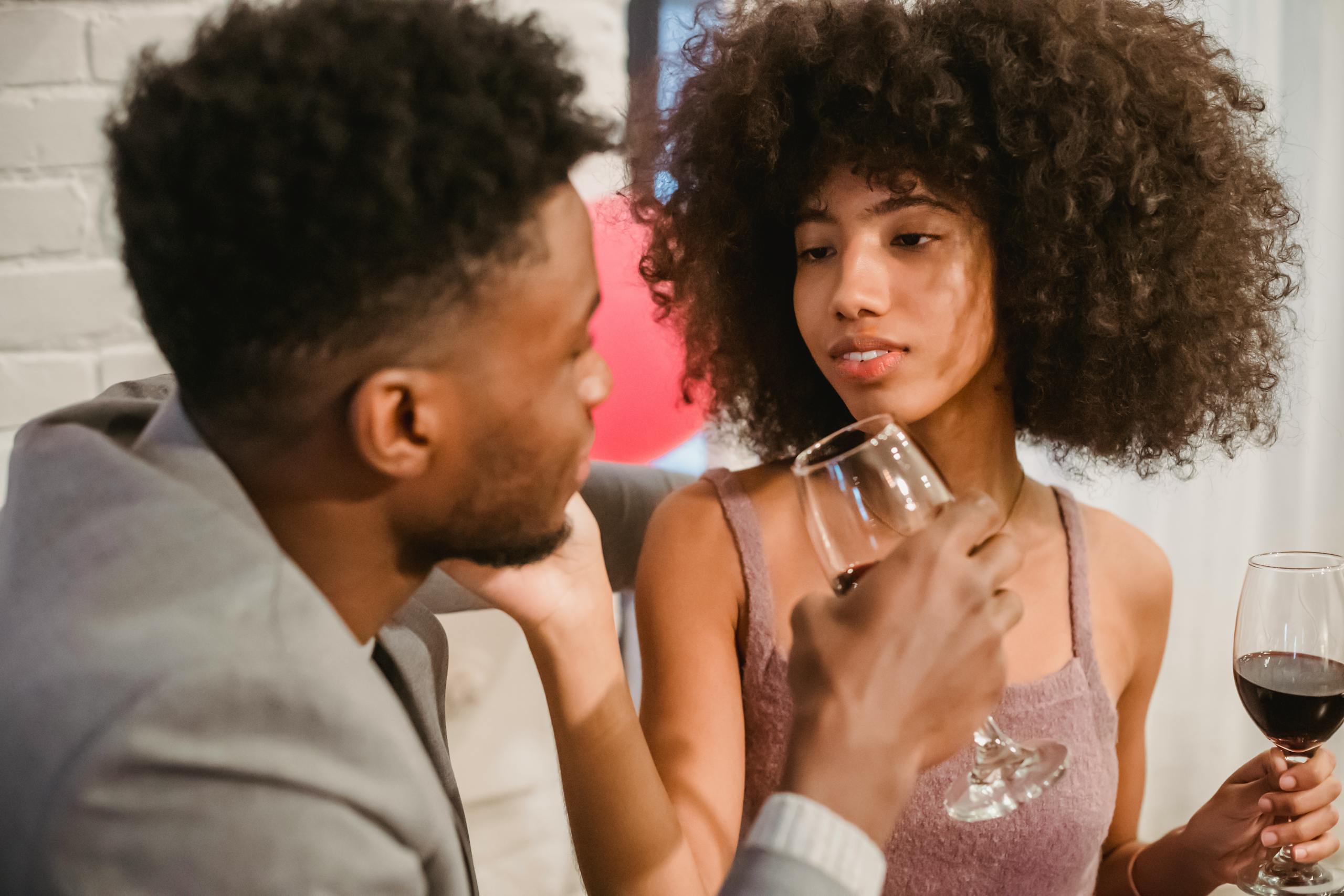 Happy young African American couple drinking wine from wineglasses and looking at each other during celebration