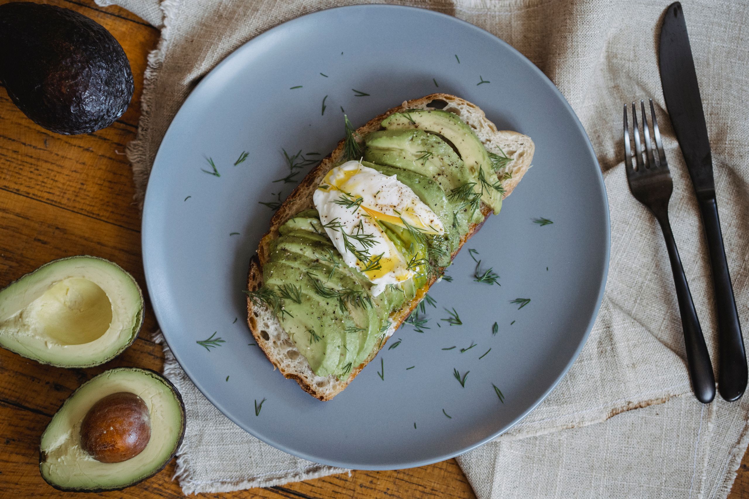 Healthy avocado toast topped with poached egg and dill on a gray plate.