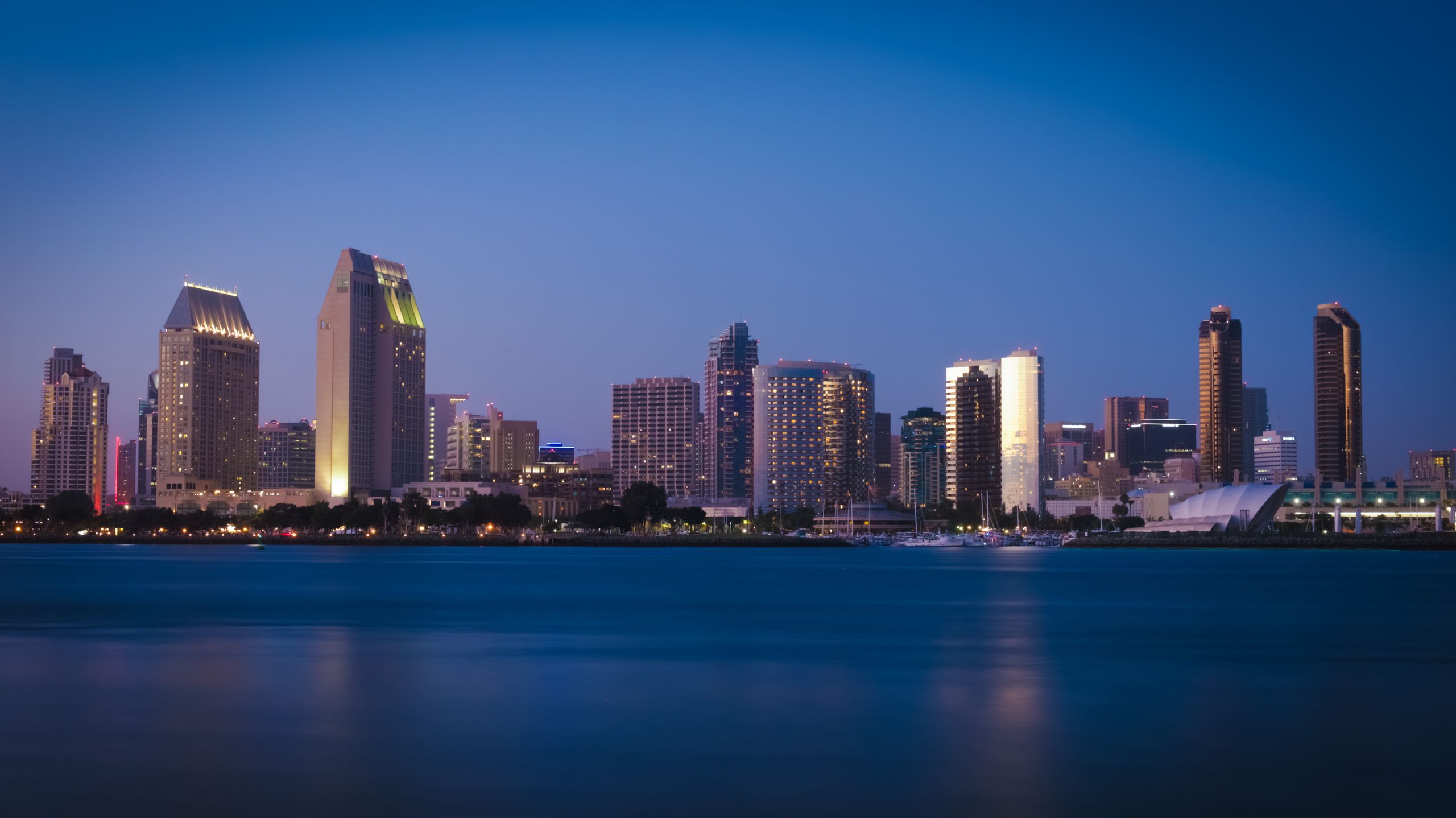 The illuminated San Diego skyline is reflecting on water at dusk, showcasing modern architecture.