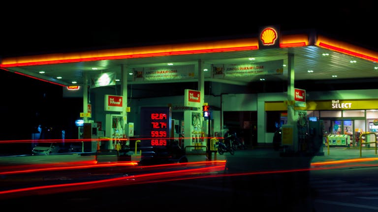 Illuminated Shell gas station with long exposure light trails at night.