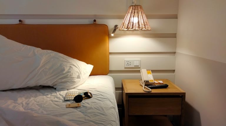 Inviting bedroom space with a lamp-lit nightstand, phone, and sunglasses on the bed.