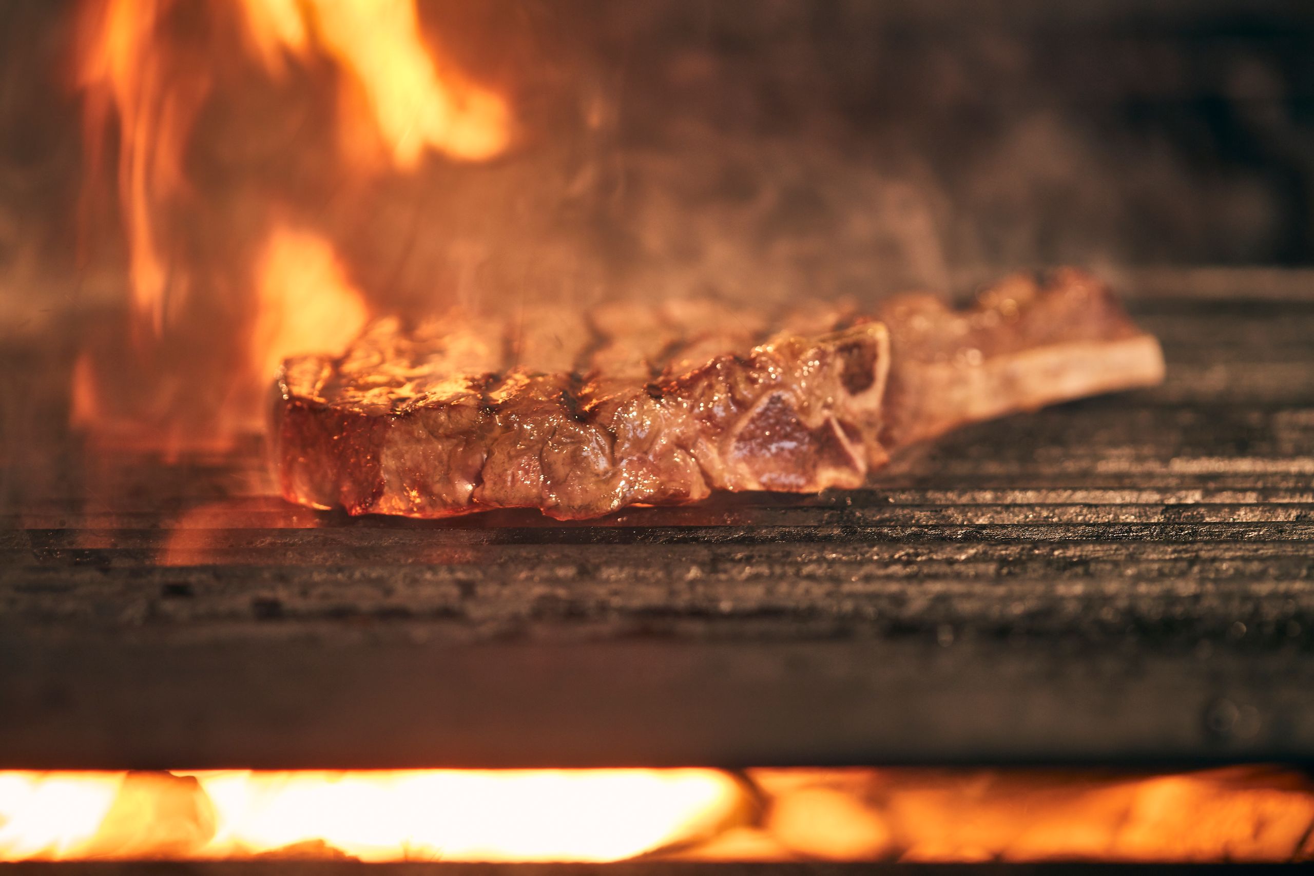 Juicy ribeye steak cooking over an open fire grill with flames, showcasing delicious grilling action.