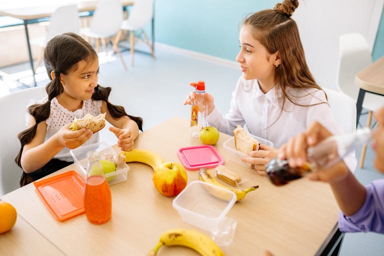 Kids having a fun lunch break with sandwiches, fruits, and drinks in a school setting.