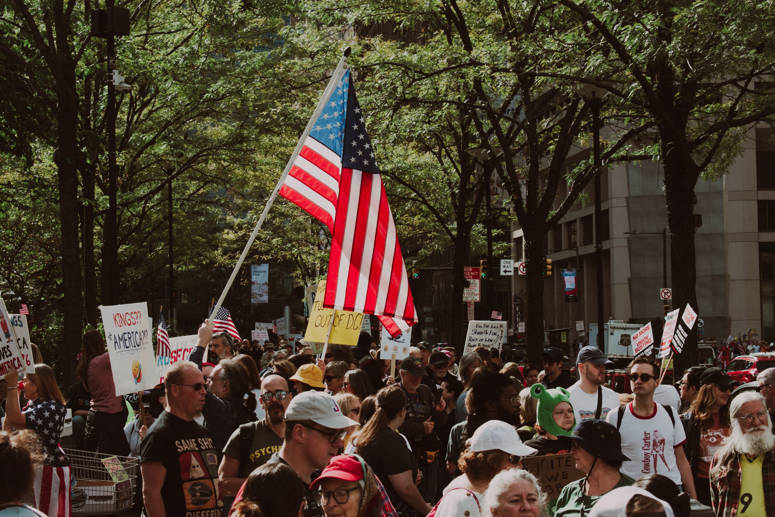 Large diverse crowd gathered outdoors for a protest holding signs and an American flag.