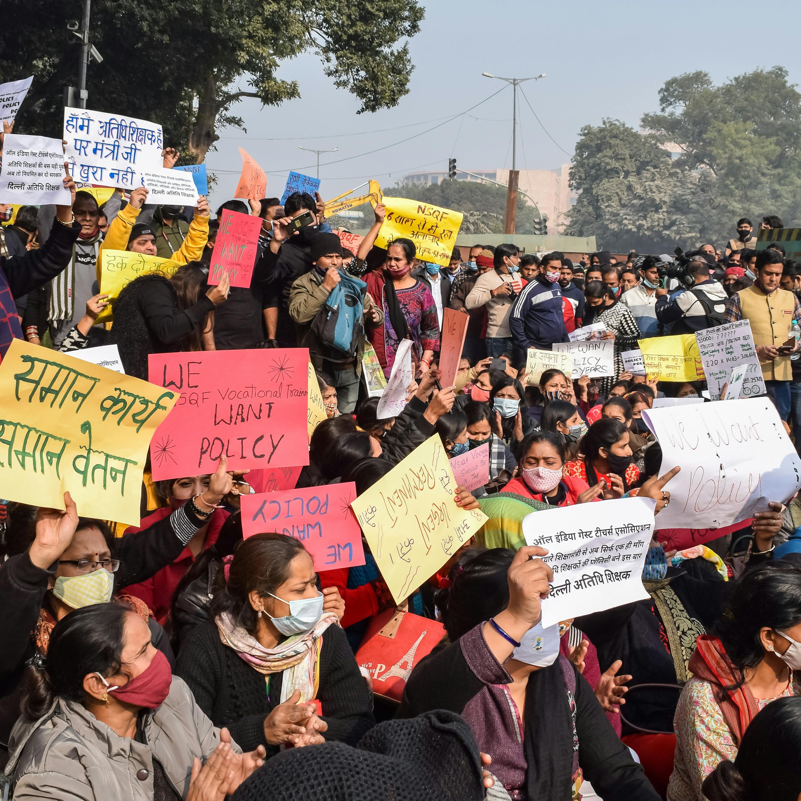 Large group of people protesting outdoors with colorful signs, demanding policy changes.