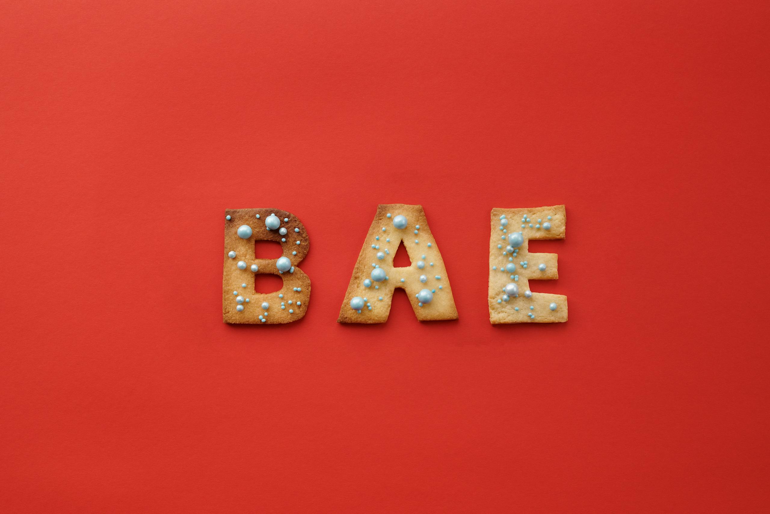 Letter-shaped cookies spelling 'BAE' adorned with sprinkles on a vibrant red background.