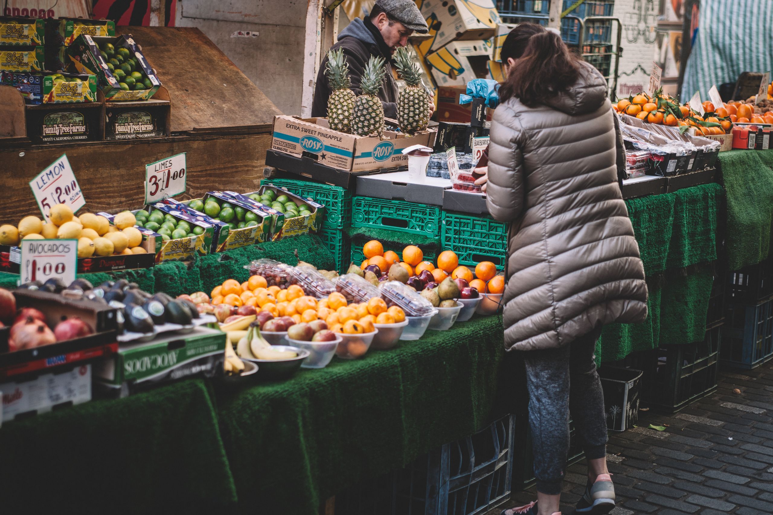 Lively city market stall displaying diverse fresh fruits. A customer browses.