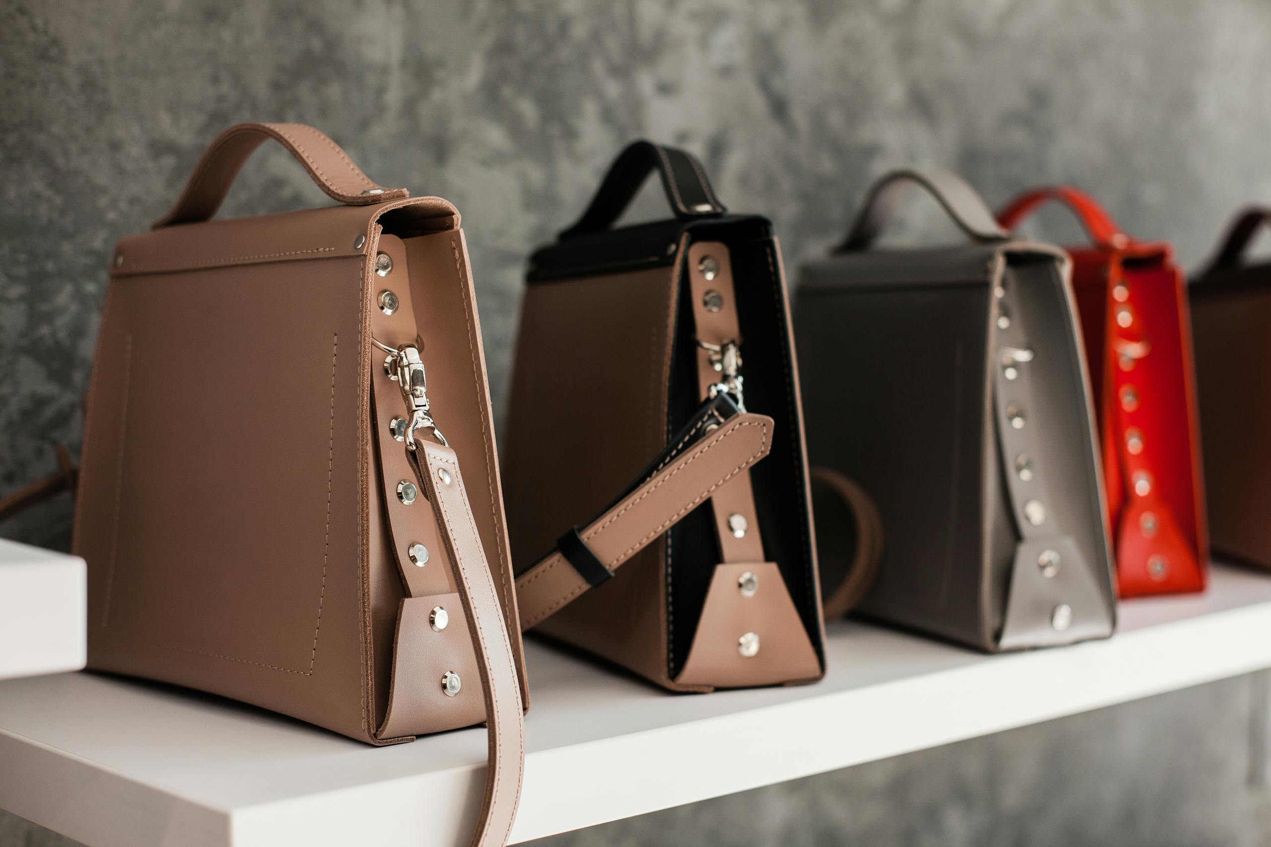 Luxury leather handbags displayed on a white shelf, showcasing minimalistic design and various colors.