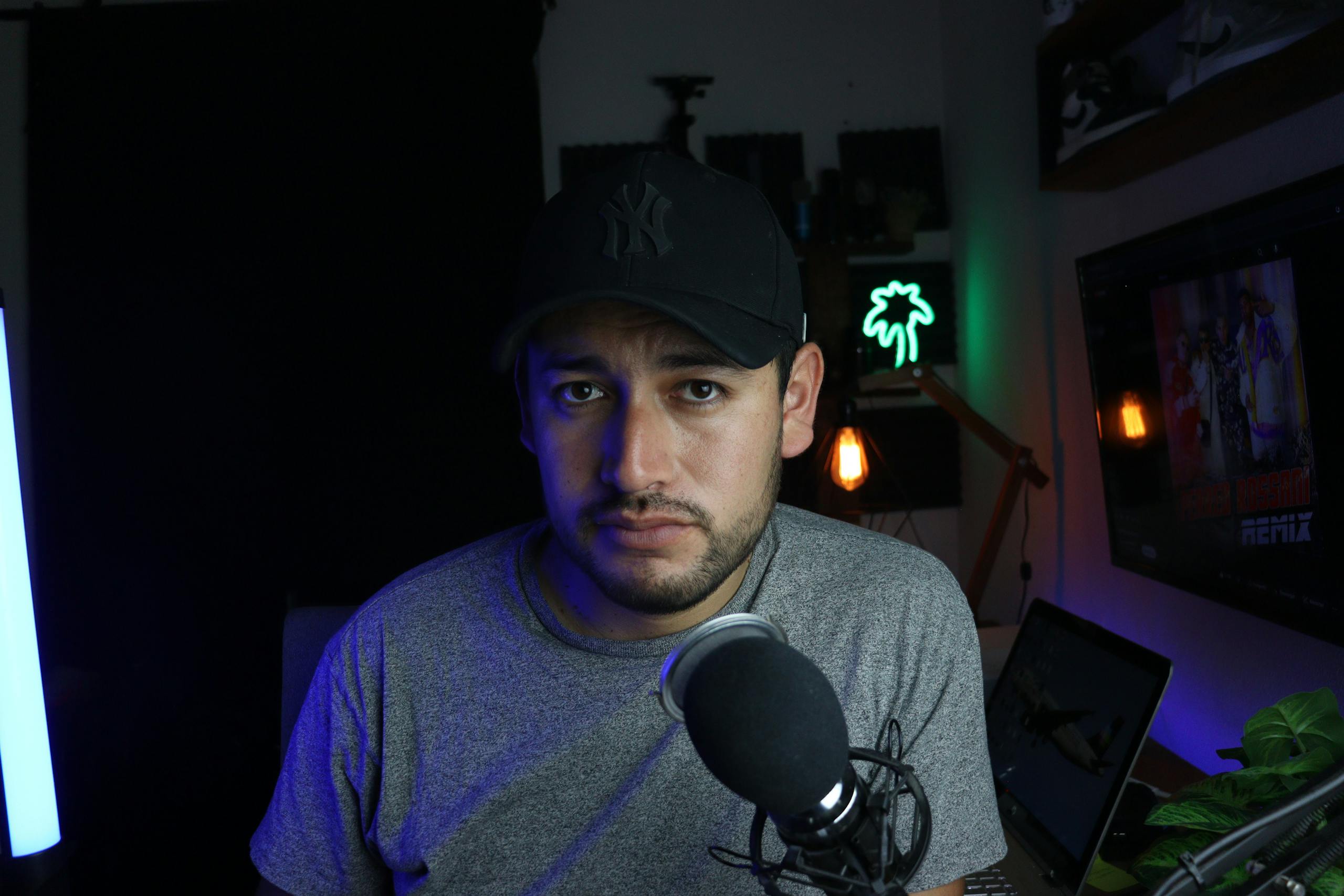 Male content creator in a home studio setup with microphone and soft lighting.