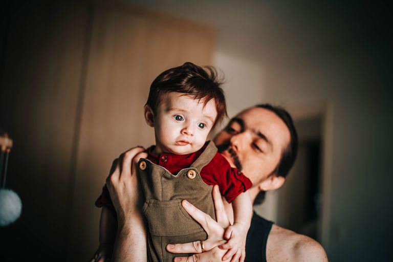 Male with mustache holding cute little boy in arms and standing in blurred room