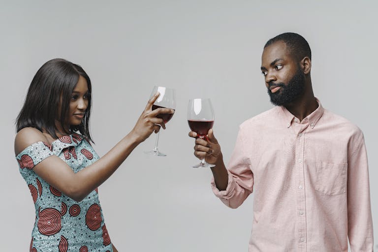 Man and woman clinking red wine glasses in a festive celebration on a white backdrop.