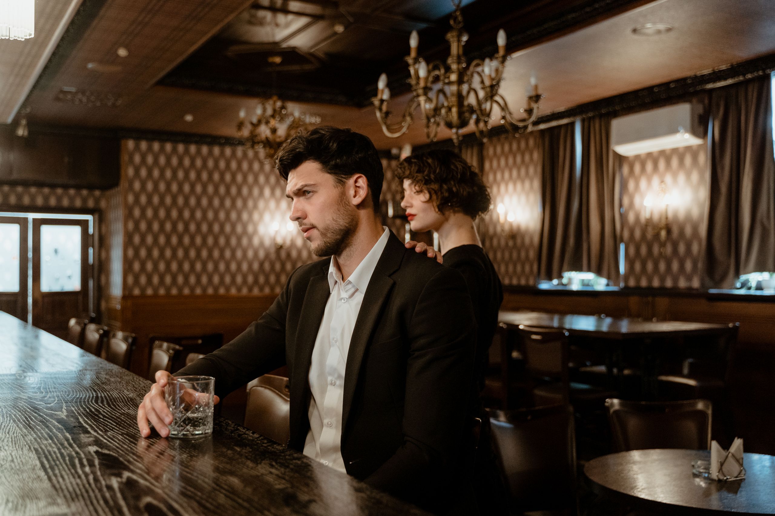 Man and woman in a classic bar, dressed elegantly, enjoying whiskey together.