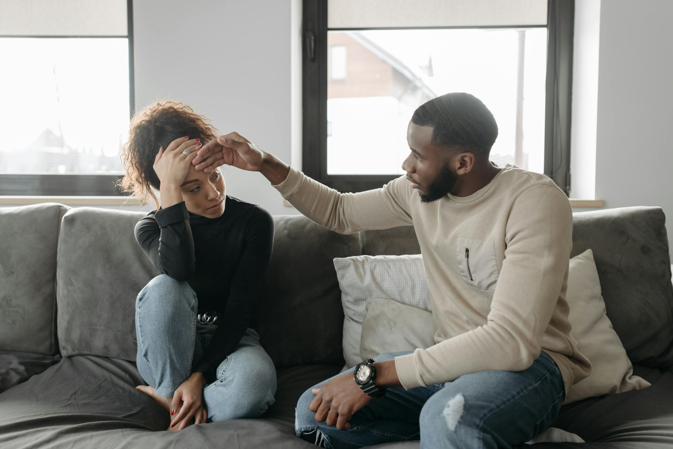 Man comforting his unwell partner on a sofa, showing concern and care indoors.