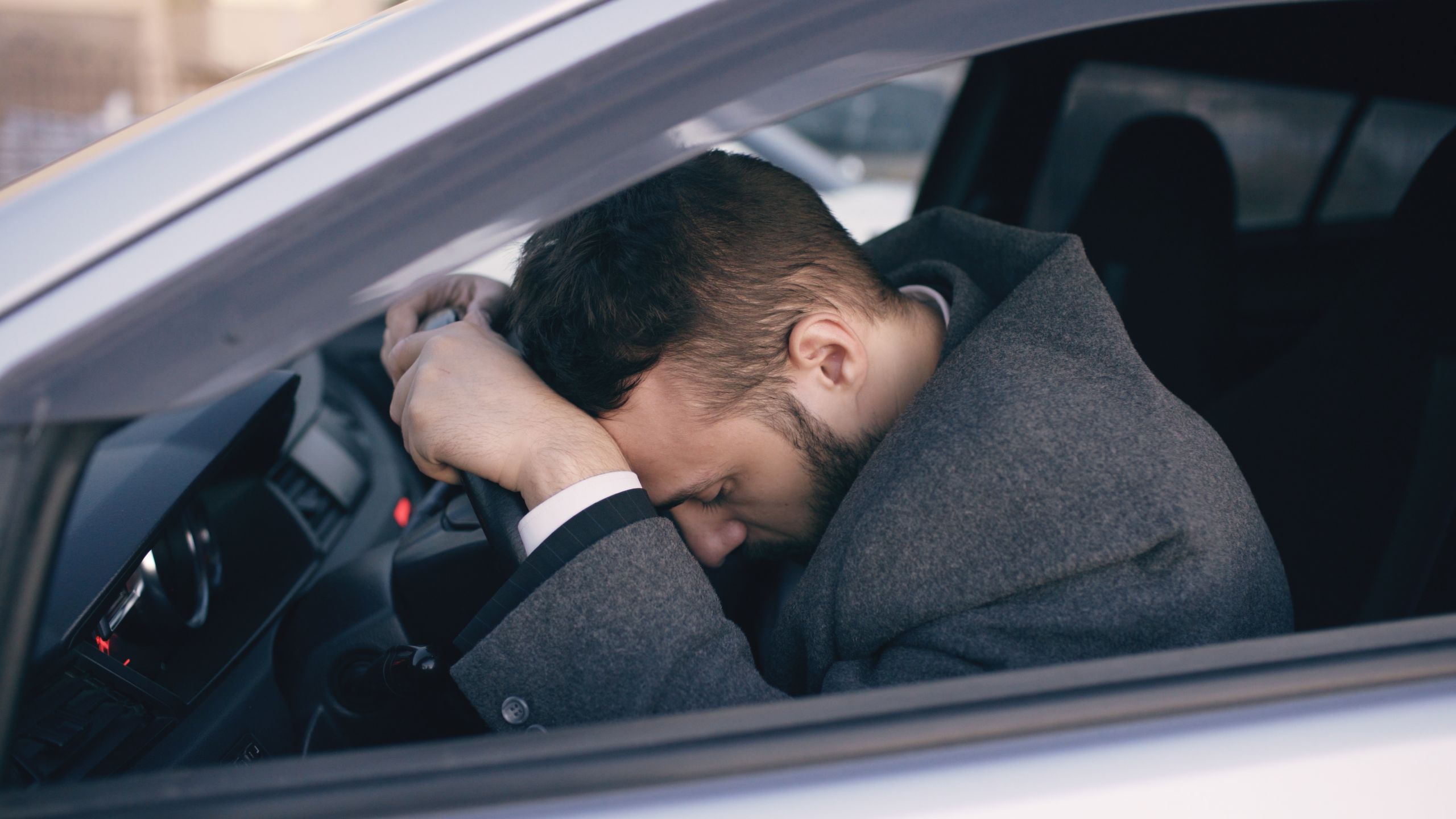 Man in car showing stress with head on steering wheel, highlighting emotional fatigue.