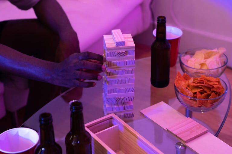 Man playing Jenga on a center table with chips and drinks during a relaxed indoor game night.