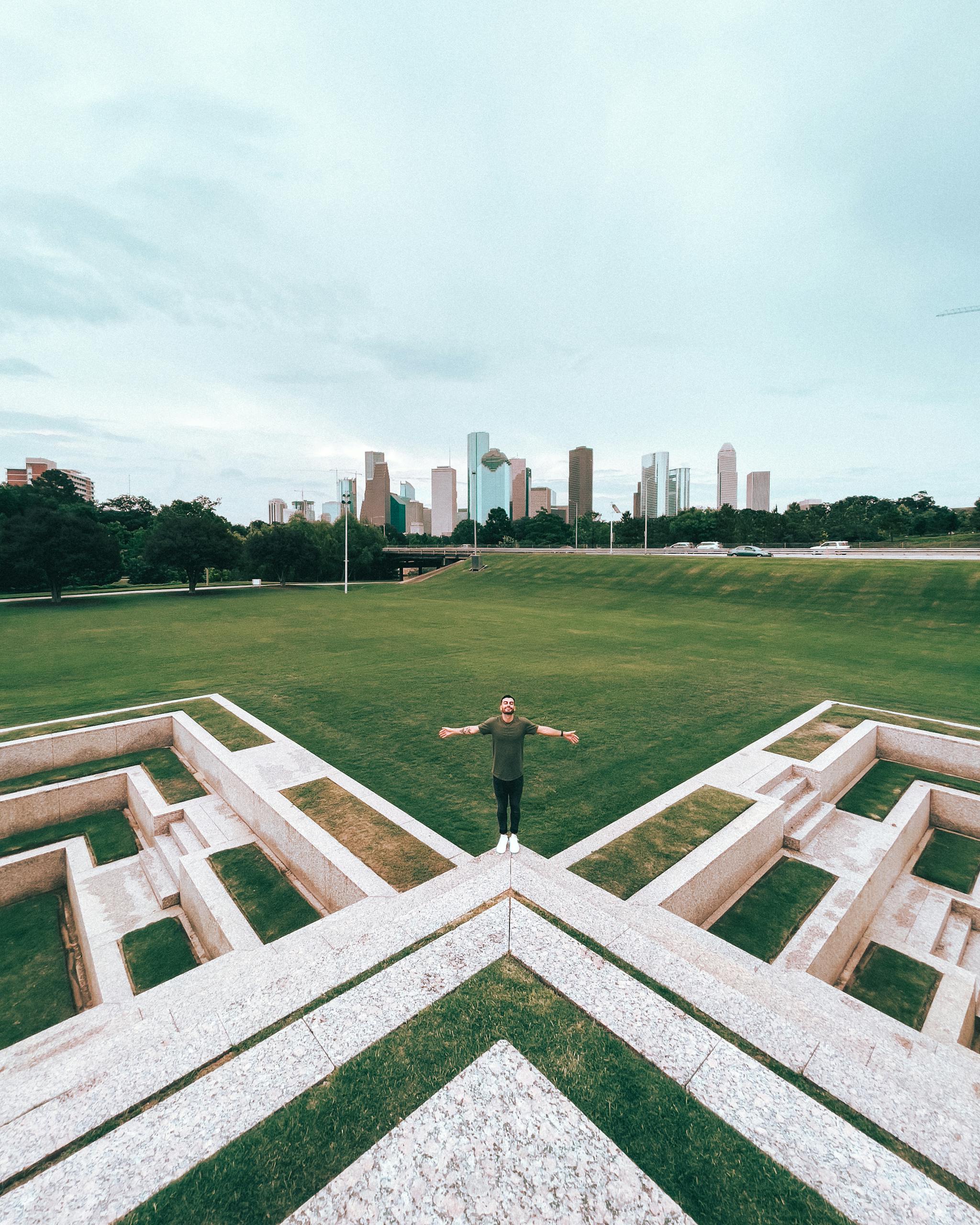 Man standing in a Houston park with a clear view of the city skyline in the background. Vibrant scenery, perfect for urban living themes.