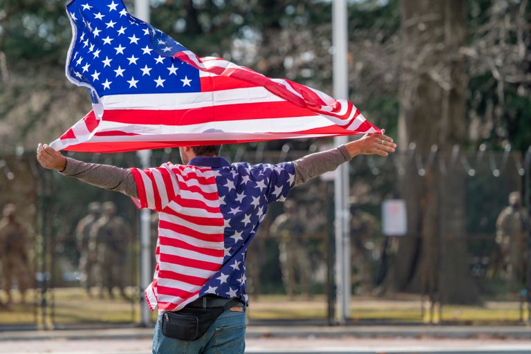 Man wearing American flag shirt and holding flag in Washington DC, symbolizing patriotism.