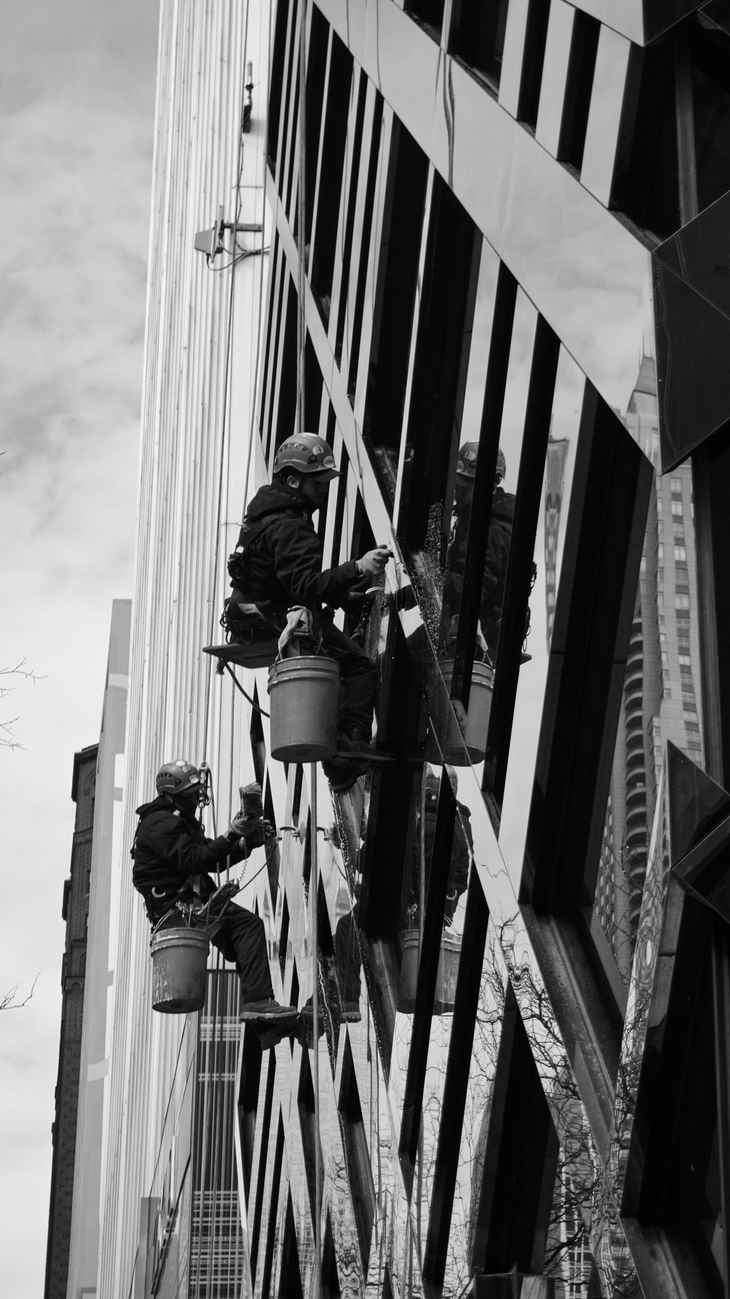 Men working as window washers on a modern skyscraper. Low angle in black and white.