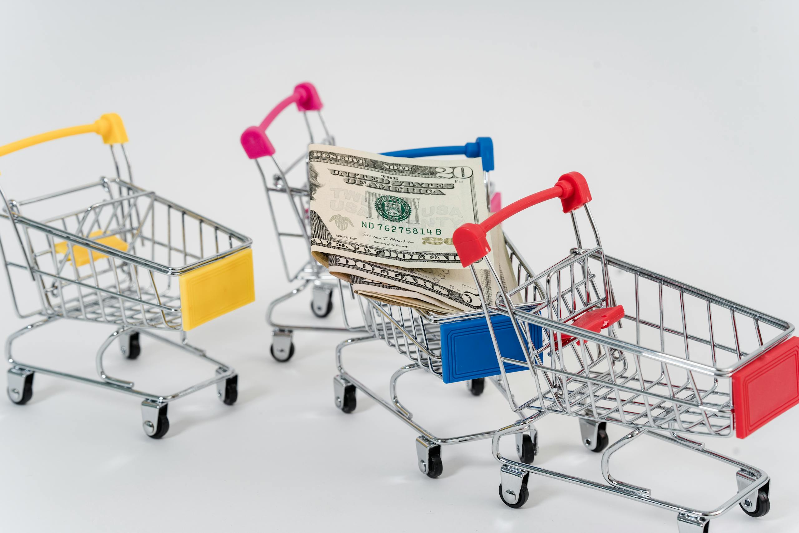 Miniature shopping carts containing dollar bills on a white background.