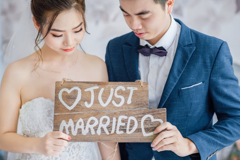 Newlywed couple in Vietnam holding a 'Just Married' sign, capturing a joyful moment.