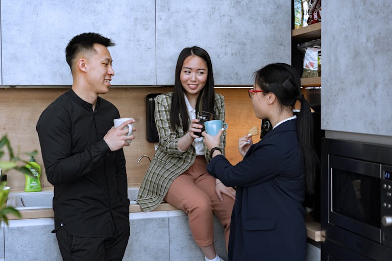 Office colleagues enjoy a coffee break in the kitchen, engaging in friendly conversation.