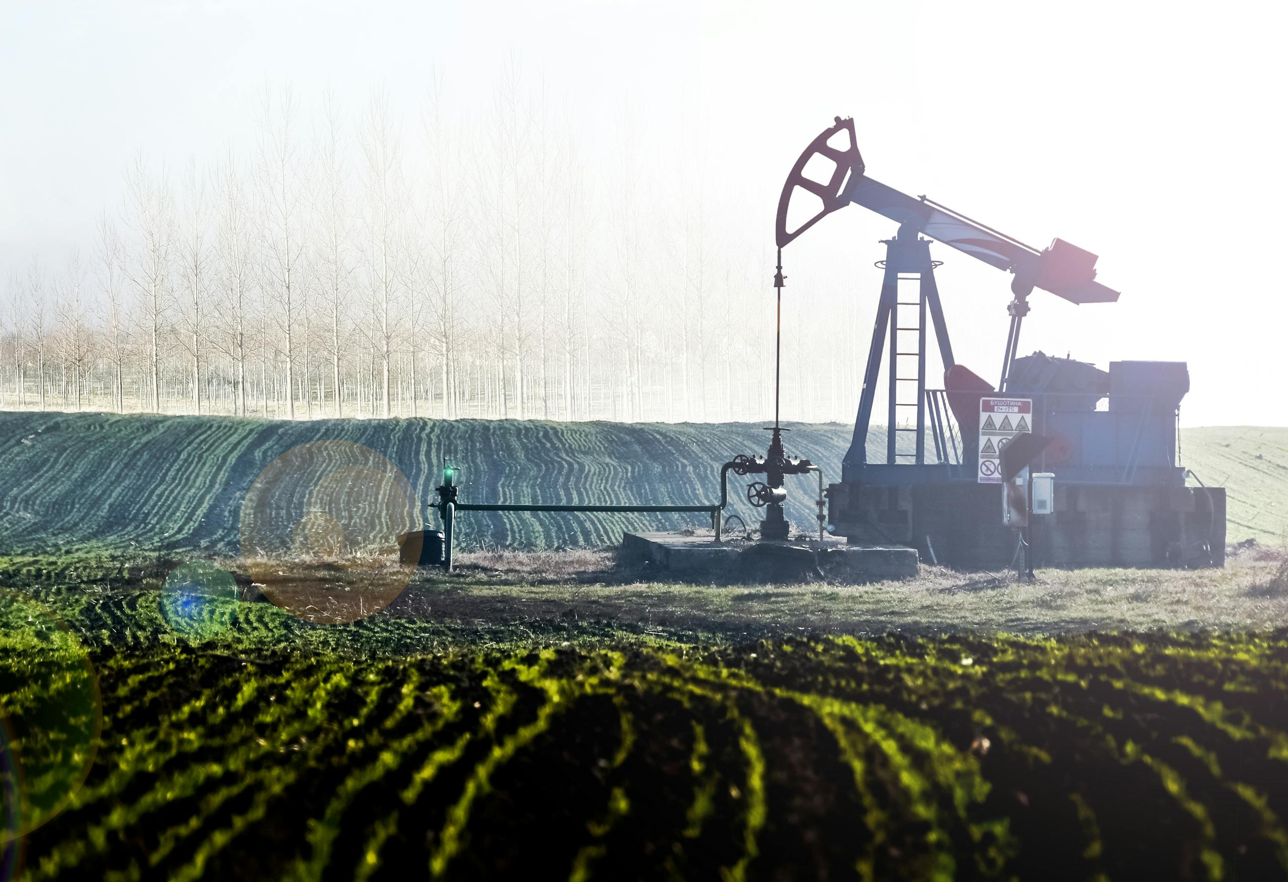 Oil pumpjack in scenic agricultural landscape with lush fields and distant trees.
