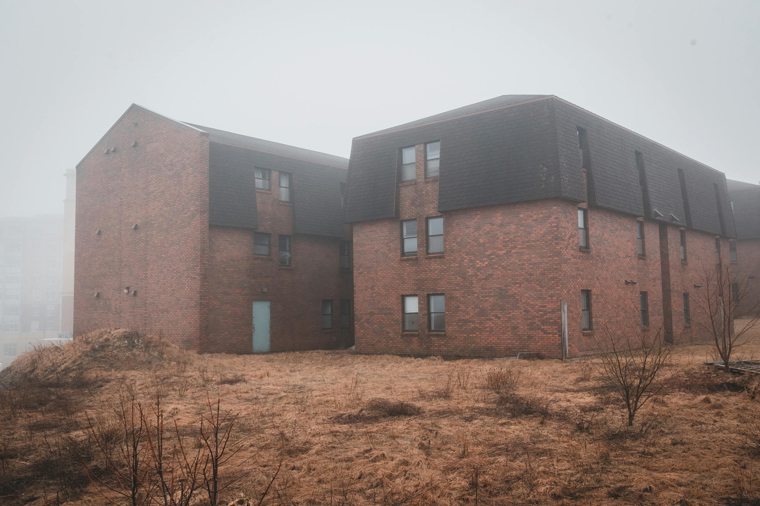 Old large brick dwelling house located in suburban district surrounded with dried grass and leafless bushes in autumn day