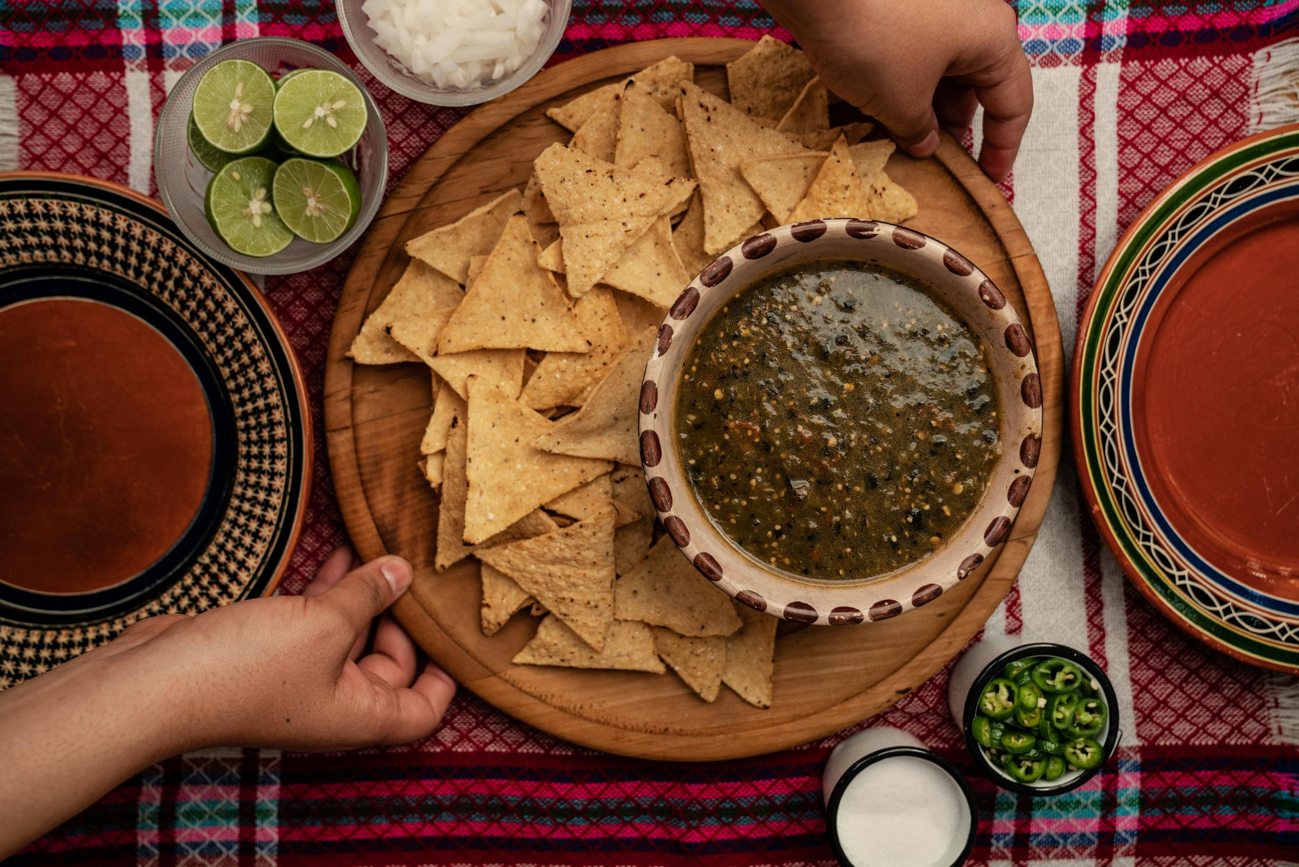 Overhead view of homemade nachos with green salsa, lime, and onions on a colorful tablecloth.