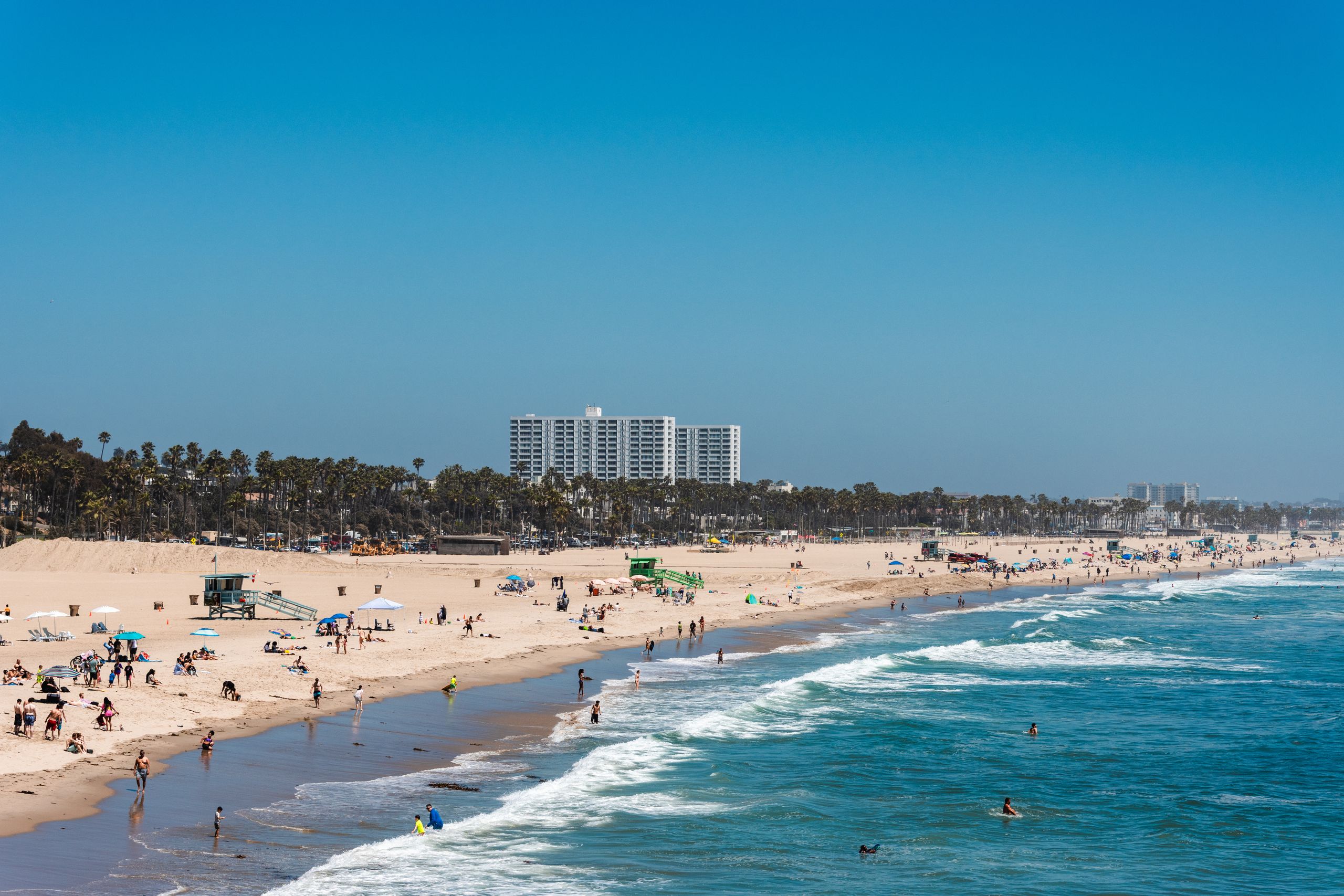 People enjoying a sunny day on Santa Monica Beach with a vibrant blue ocean in Los Angeles.