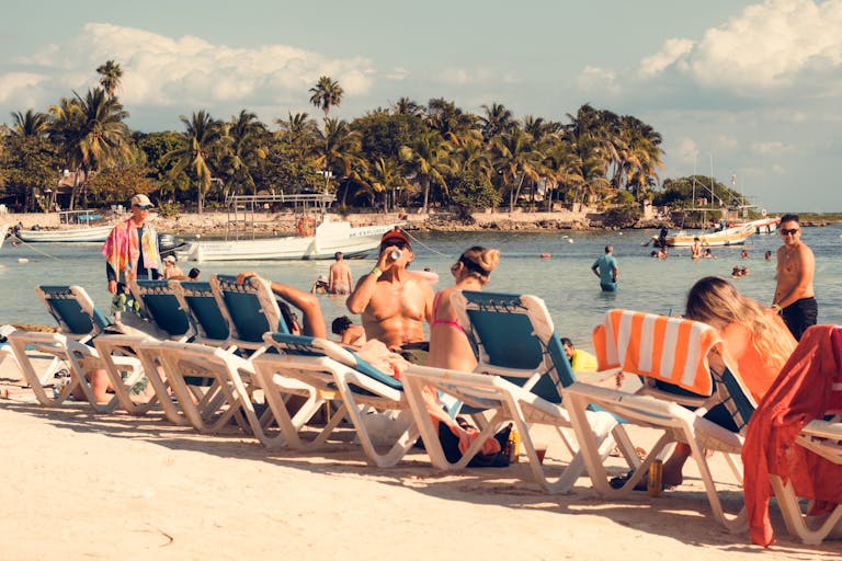 People enjoying a tropical beach with sunbeds, ocean view, and palm trees in summer.