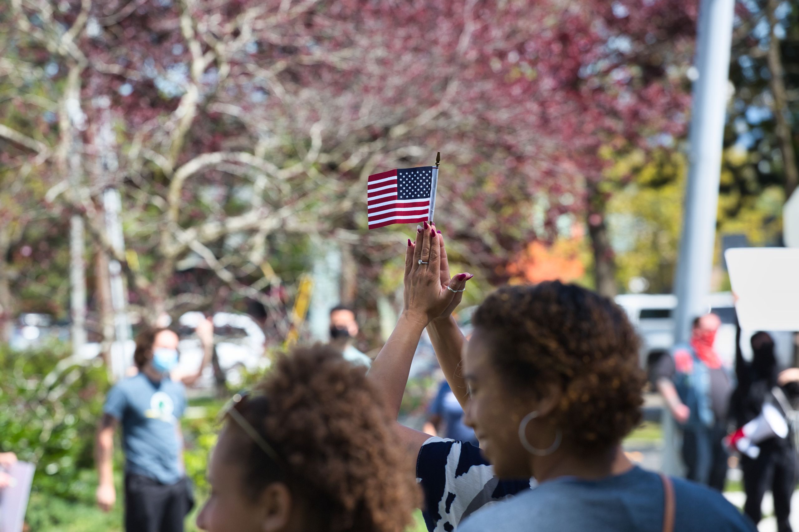 People gathered outdoors waving a small American flag in Bellingham, WA.