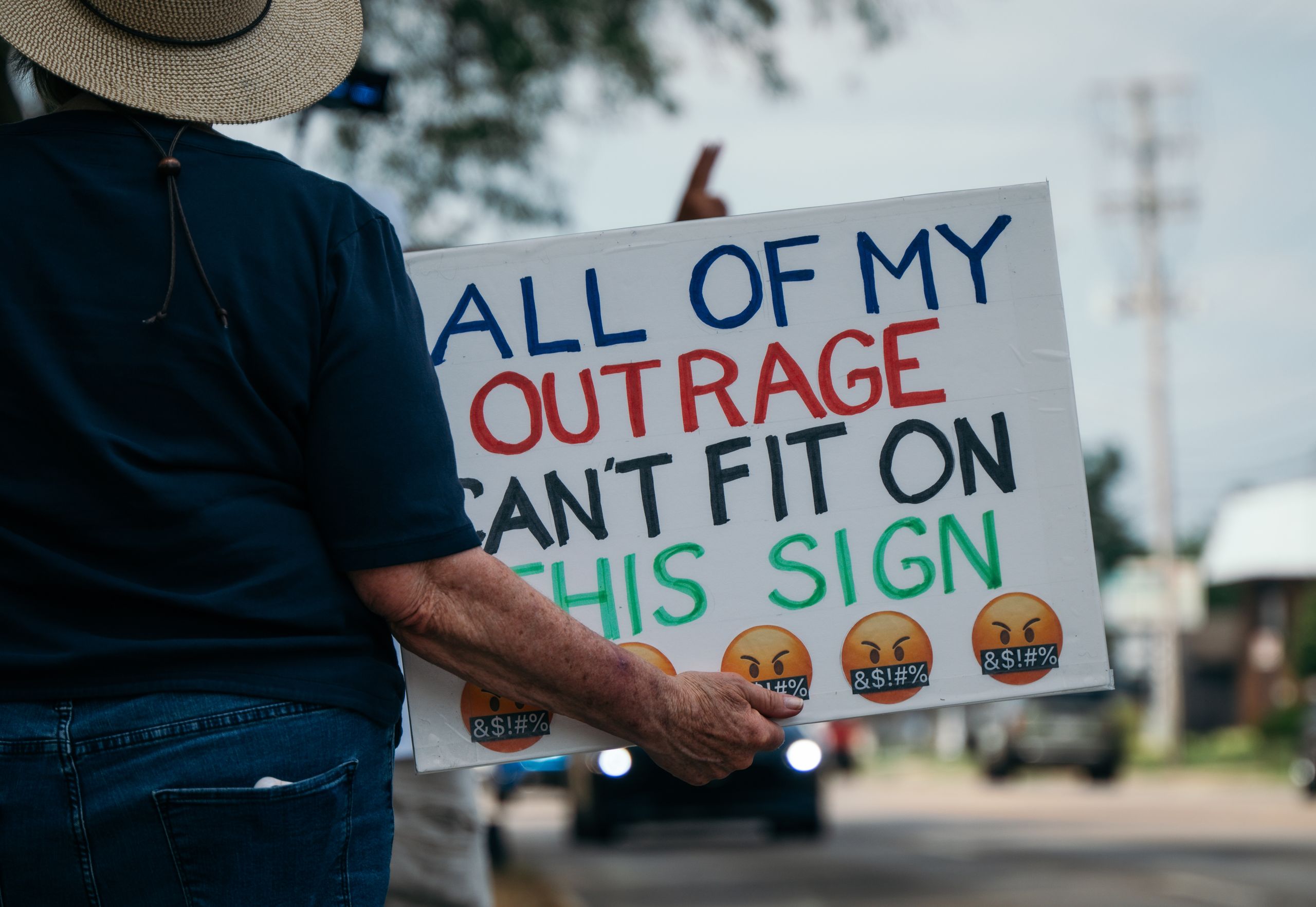 Person at a protest holding a sign expressing their outrage. Outdoors setting.