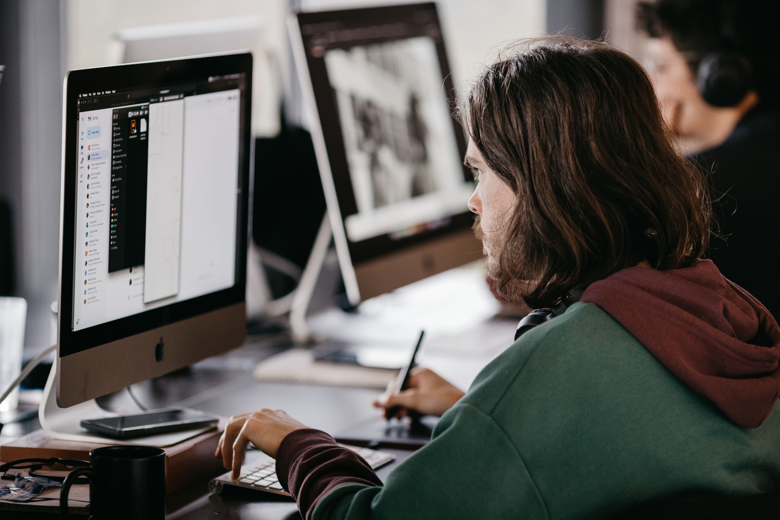 Person in a hoodie working at a desktop computer in an office setting, focused and engaged.