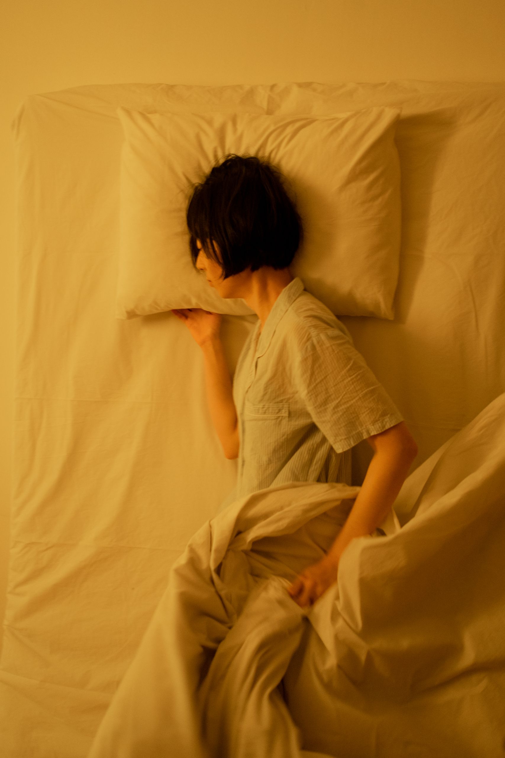 Person in pajamas peacefully sleeping on a bed with soft white linens.