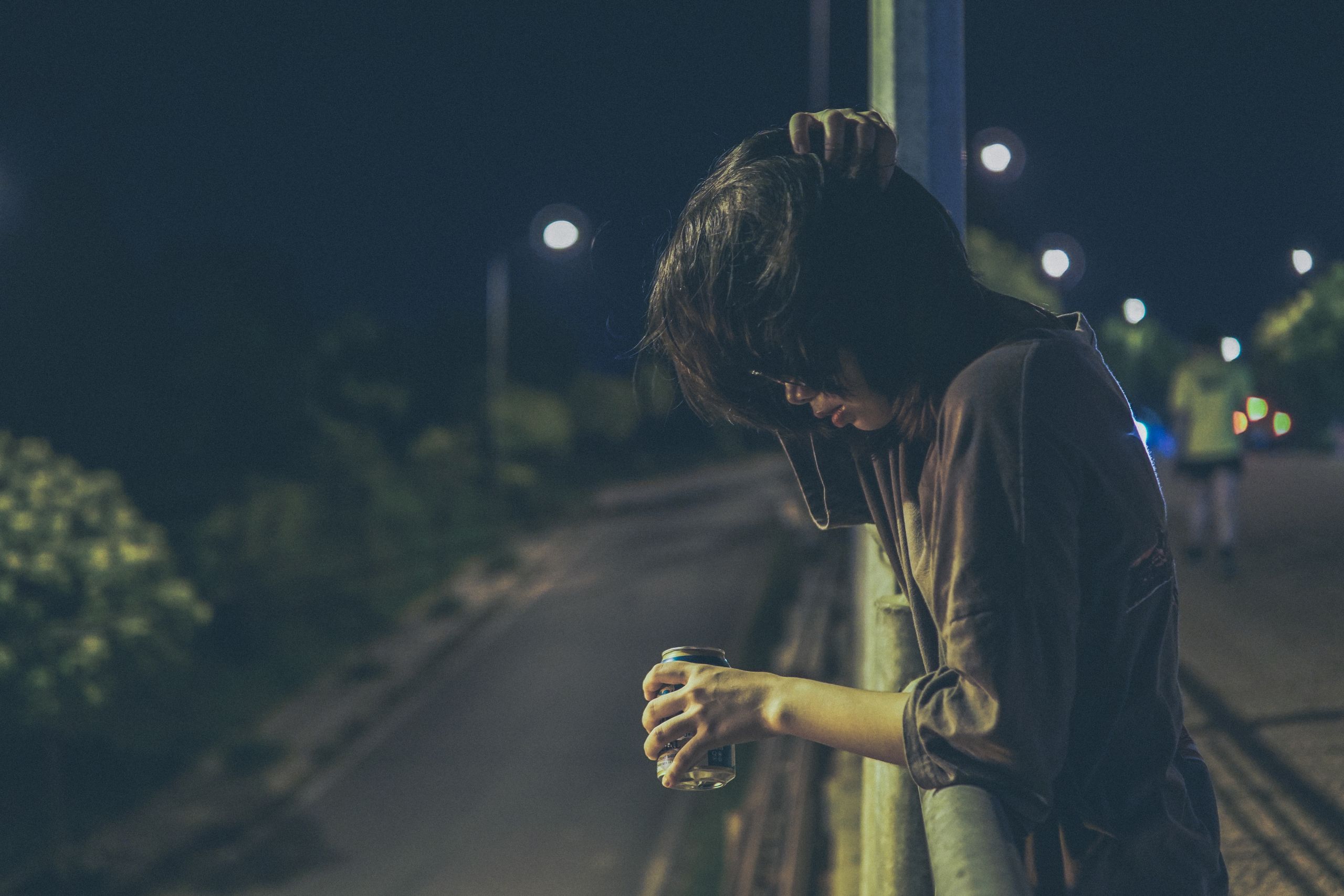 Person standing alone at night, leaning with a drink, capturing a contemplative mood.