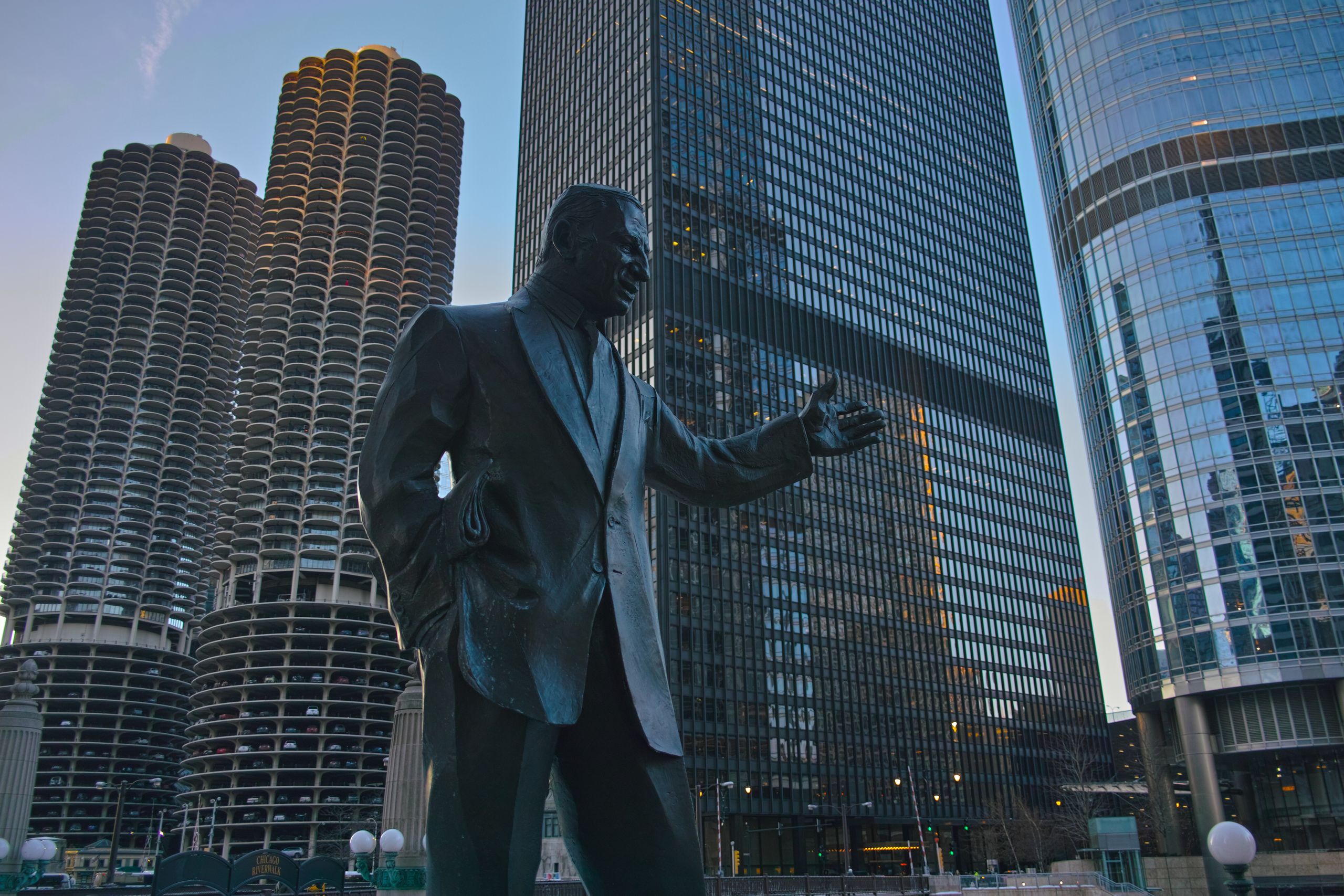 Photograph of Irv Kupcinet statue against Chicago's iconic skyscrapers during the day.