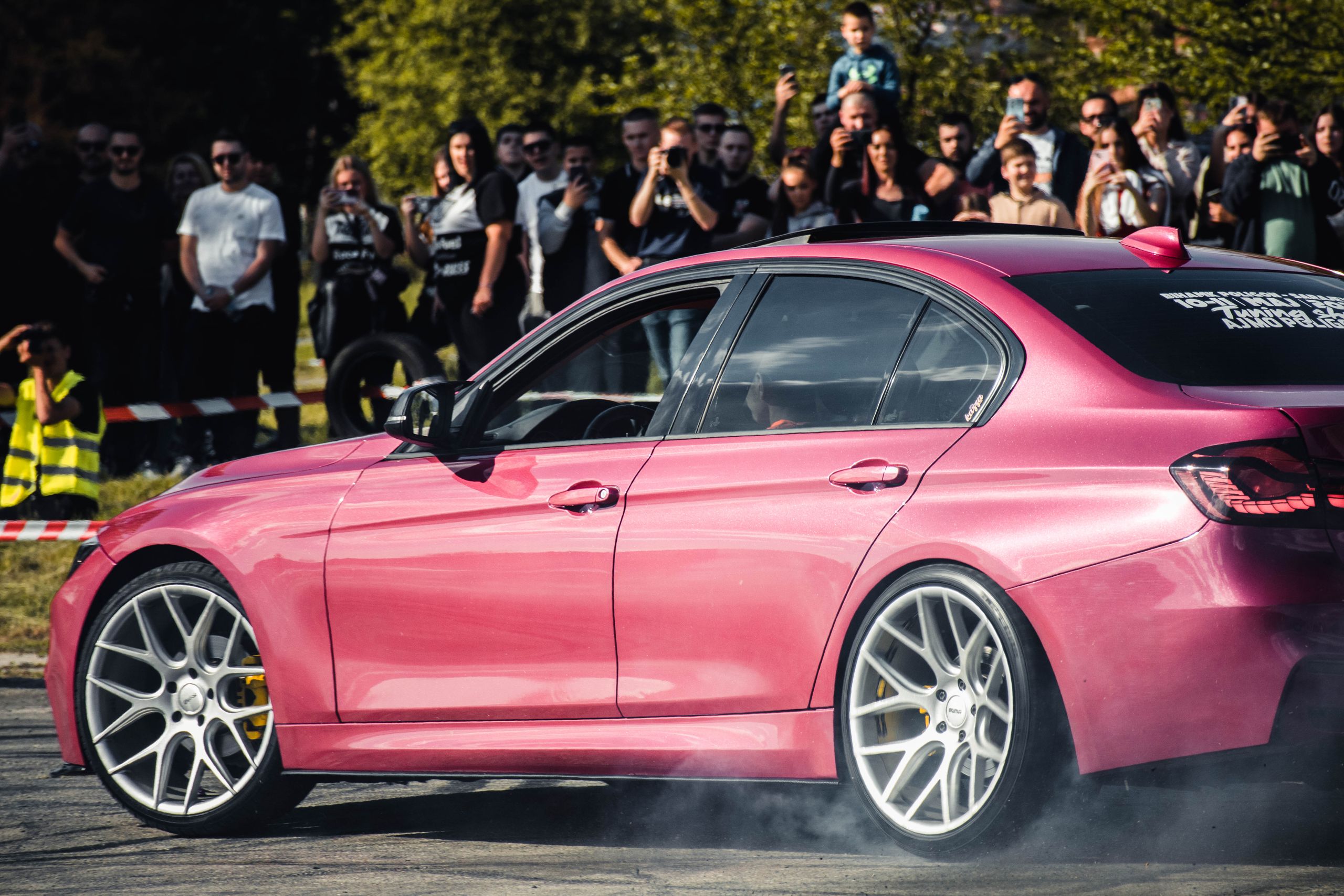 A pink sports sedan was showcased at Sarajevo auto event with an audience enjoying the performance.