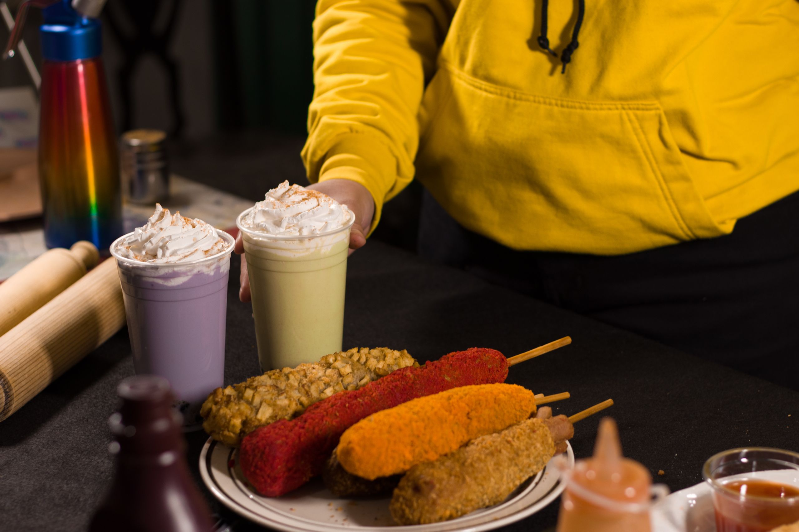 Plate of colorful corn dogs with whipped cream milkshakes on a black table setting.