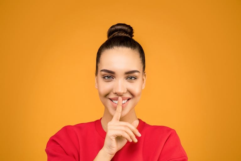 Portrait of a smiling woman making a quiet gesture against a vibrant background.