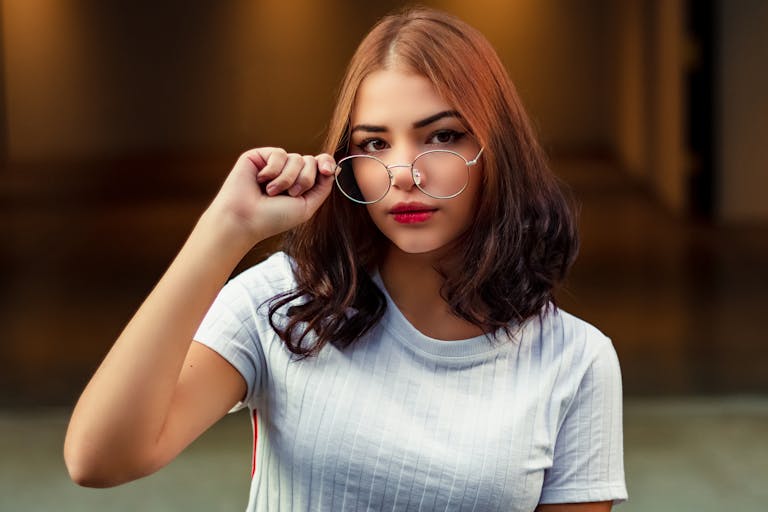 Portrait of a stylish young woman adjusting her eyeglasses indoors, exuding confidence and elegance.